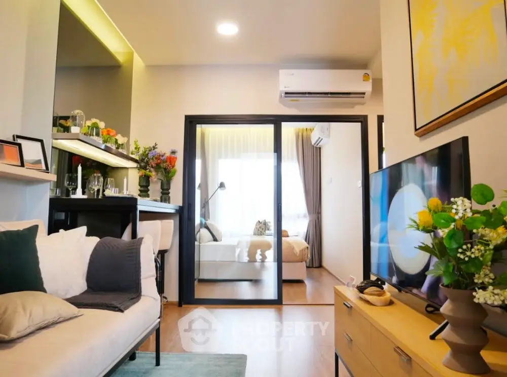 Modern living room with open layout and stylish decor, featuring a cozy bedroom view through sliding glass doors.