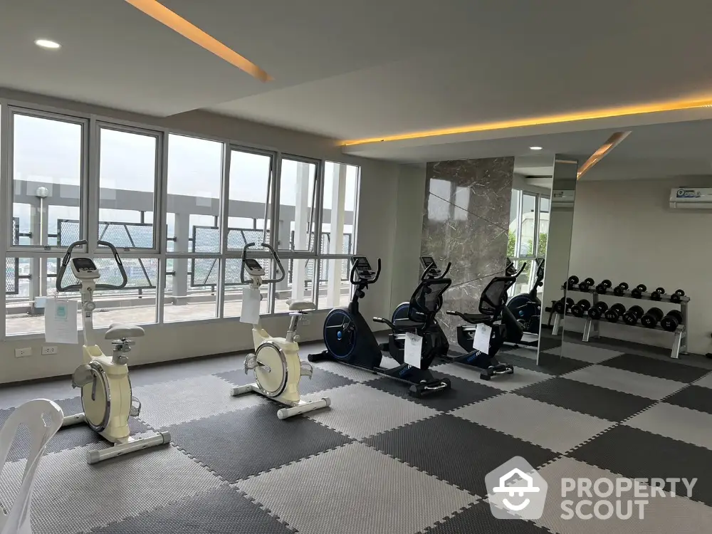 Modern gym with exercise bikes and weights in a high-rise building with city view.