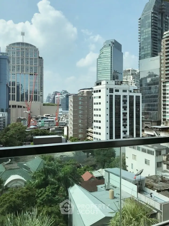 Stunning cityscape view from a modern balcony with glass railing, showcasing urban architecture and greenery.
