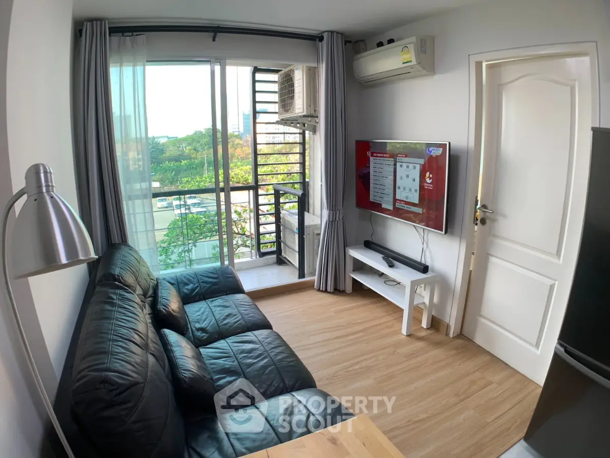 Modern living room with balcony view, black leather sofa, and wall-mounted TV in a cozy apartment.