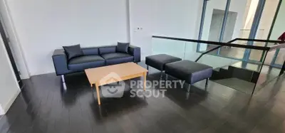 Modern living room with sleek black sofa and glass railing, featuring dark wood flooring.