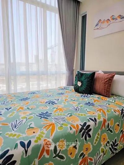 Bright bedroom with floral bedding and large window offering city view.