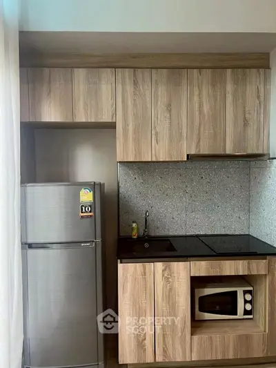 Modern compact kitchen with wood cabinets, fridge, and built-in microwave in a stylish apartment.