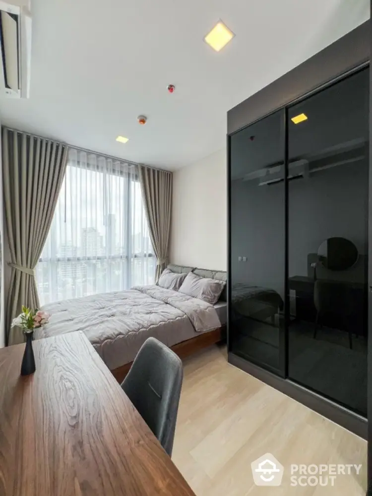 Modern bedroom with city view, featuring sleek furniture and large windows for natural light.