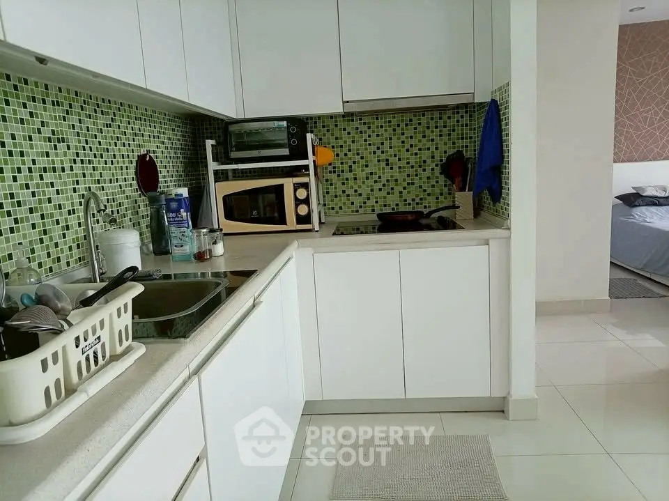 Modern kitchen with sleek white cabinets and mosaic tile backsplash, featuring a compact layout and appliances.