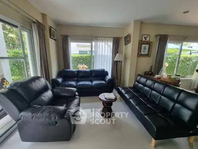 Spacious living room with leather sofas and large windows offering garden views.
