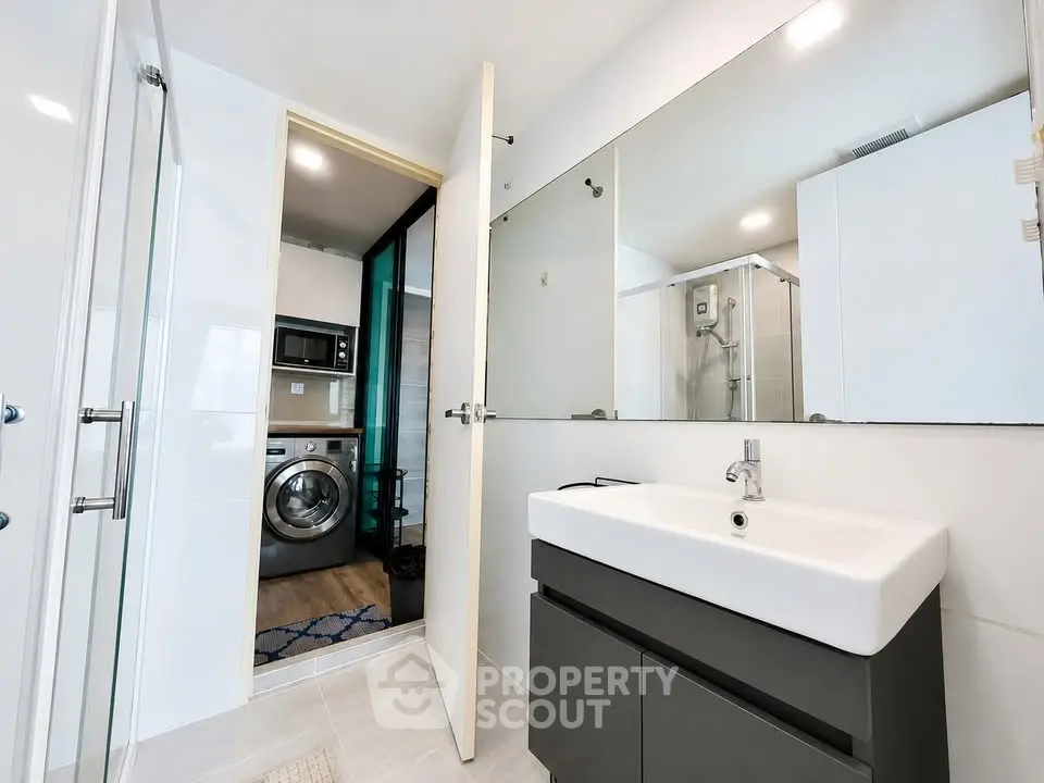 Modern bathroom with sleek sink and washing machine in adjacent laundry area.