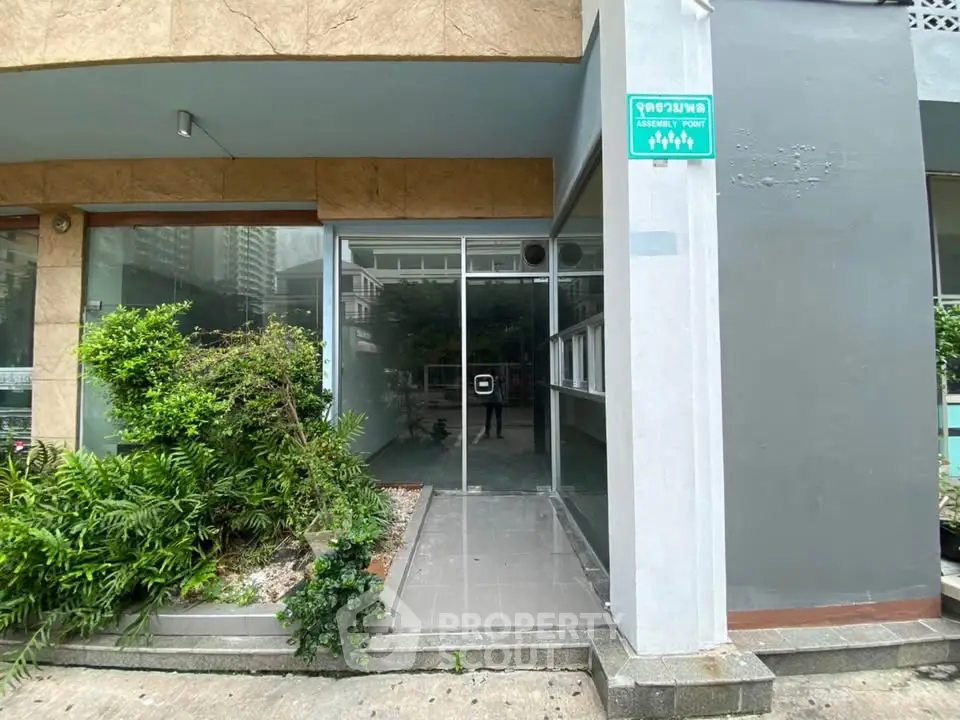 Modern building entrance with glass doors and lush greenery