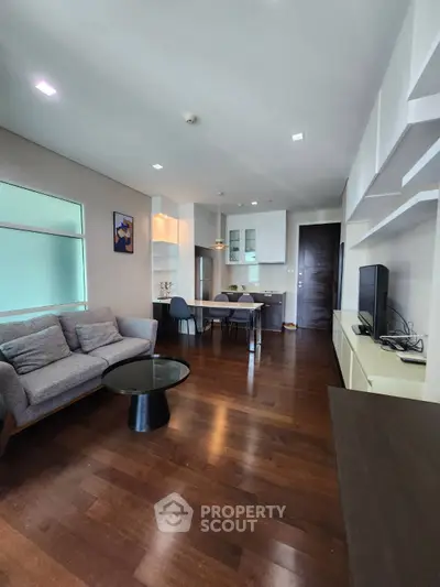 Modern living room with sleek furniture and open kitchen layout, featuring hardwood floors and stylish decor.