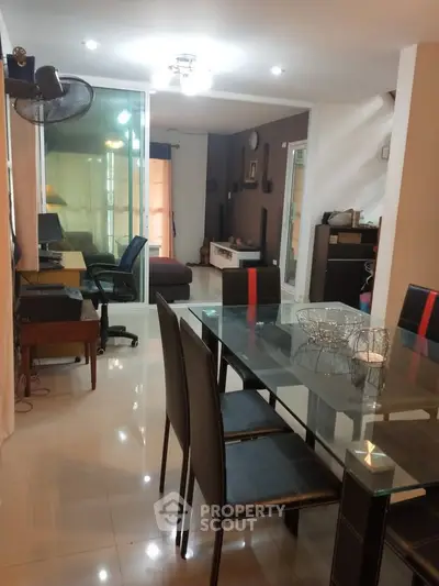Modern dining area with glass table and sleek black chairs, adjacent to cozy living space.