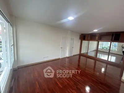 Spacious empty room with polished wooden floors and large windows in modern apartment.