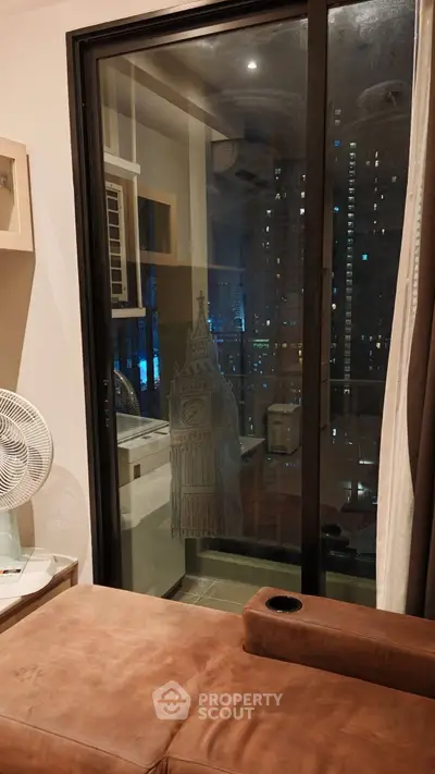 Cozy living room with city view through glass door, featuring a comfortable sofa and modern decor.