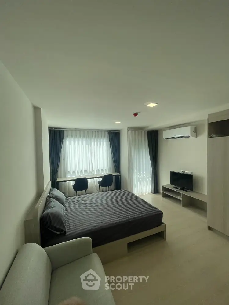 Modern bedroom with stylish decor, featuring a cozy bed, sleek furniture, and natural light from large windows.