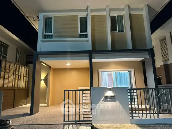 Modern two-story house with sleek design and illuminated entrance at night.