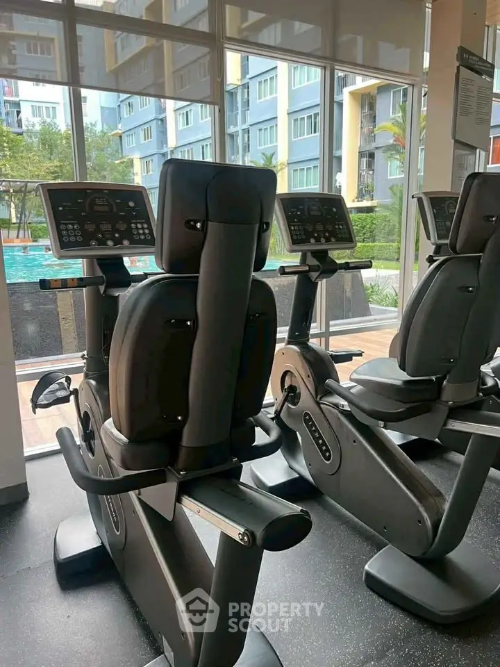 Modern gym with exercise bikes and pool view in luxury apartment complex.