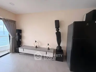 Modern living room with sleek decor and ocean view balcony, featuring elegant sculptures and a large refrigerator.
