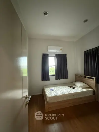 Cozy bedroom with wooden flooring and natural light, featuring a comfortable bed and air conditioning.