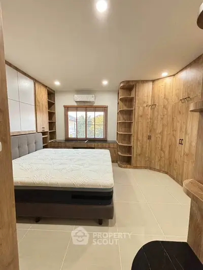 Spacious bedroom with modern wooden built-in furniture and large window view.