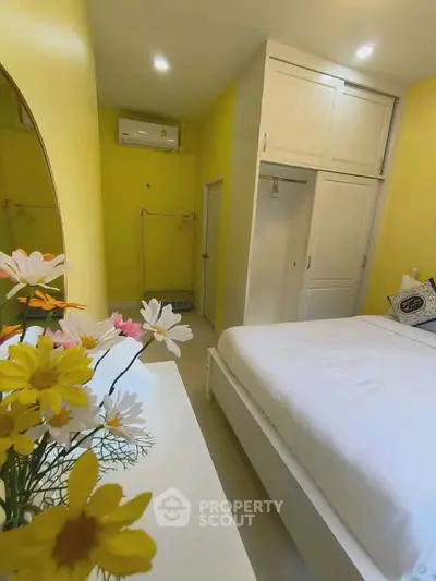 Bright yellow bedroom with white furniture and floral decor, featuring a cozy ambiance.