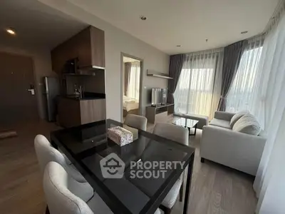 Modern living room with open kitchen and dining area, featuring large windows and stylish furniture.