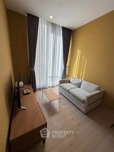 Cozy living room with high ceilings, modern sofa, and natural light from tall windows.