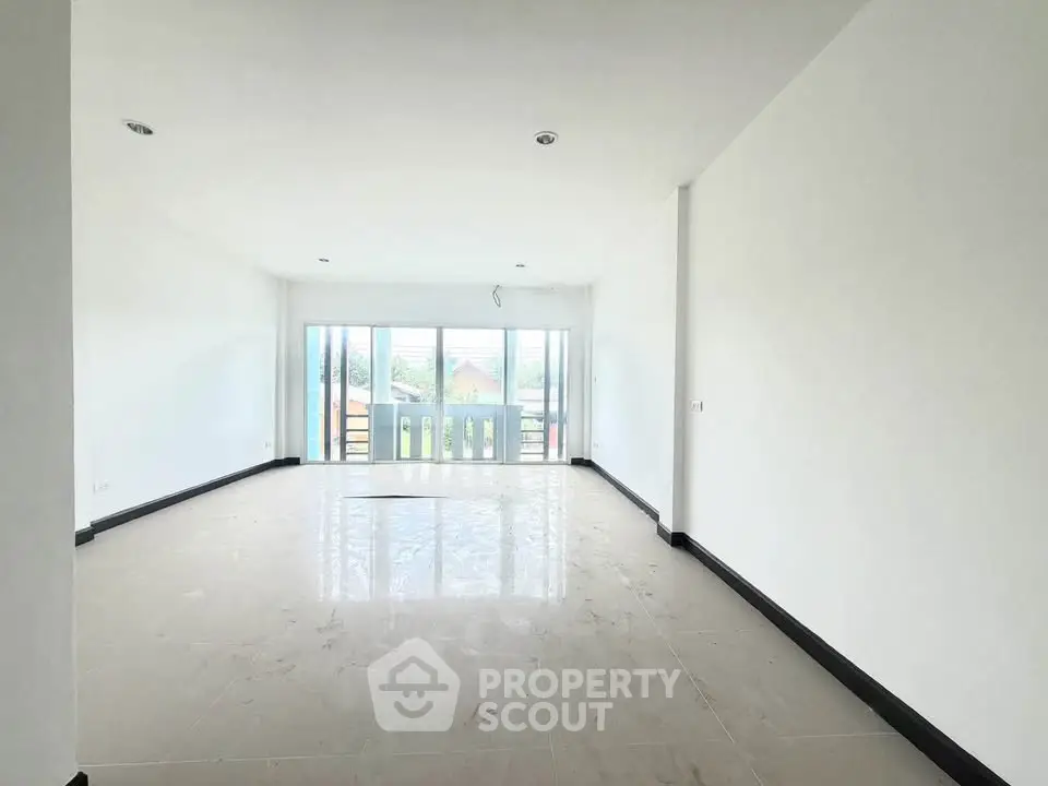 Spacious empty living room with large windows and balcony access, offering abundant natural light and open space.