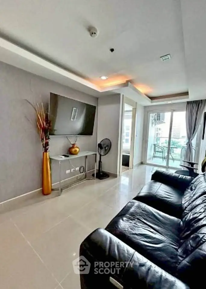 Modern living room with sleek leather sofa and wall-mounted TV, featuring a bright balcony view.