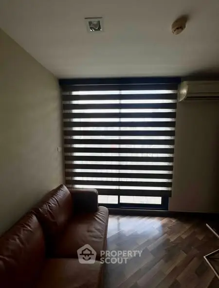 Cozy living room with modern blinds and leather sofa, featuring wooden flooring and air conditioning.