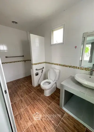 Spacious modern bathroom with wooden flooring and sleek fixtures.
