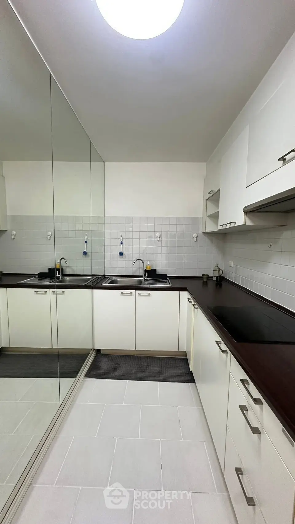 Modern kitchen with sleek white cabinets and mirrored wall for spacious feel.