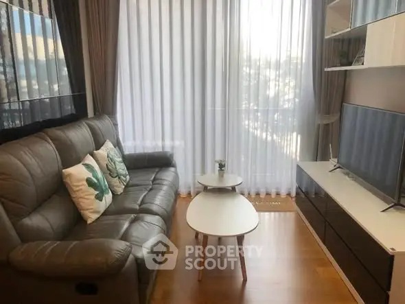 Cozy living room with leather sofa, modern TV unit, and natural light through sheer curtains.