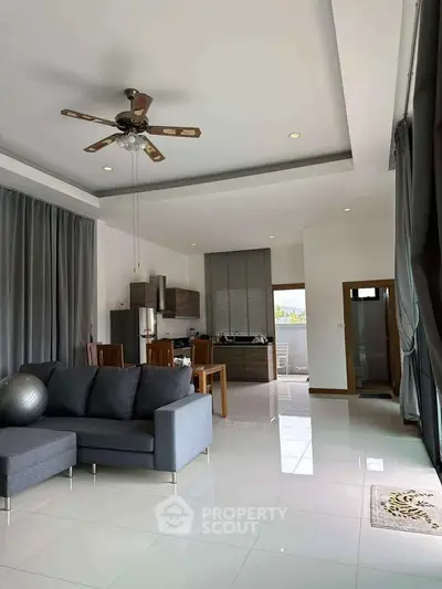 Spacious modern living room with open kitchen, featuring sleek furniture and ceiling fan.