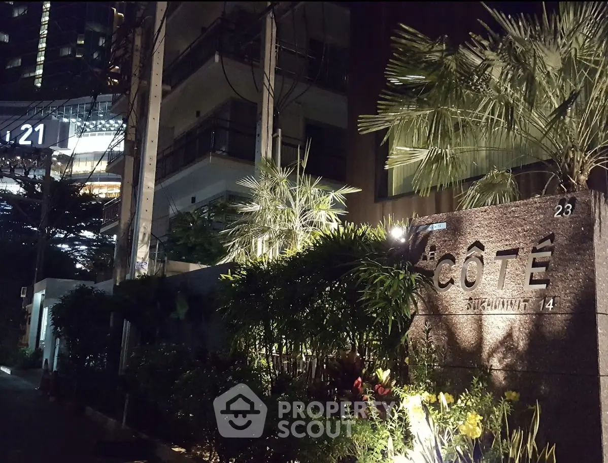 Elegant nighttime view of a modern apartment building entrance with lush greenery.