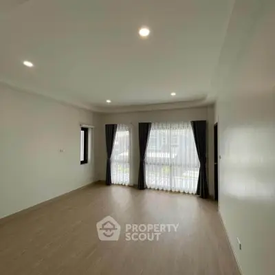 Spacious empty living room with large windows and wooden flooring.