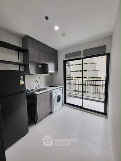 Modern kitchen with washing machine and balcony access in sleek apartment.