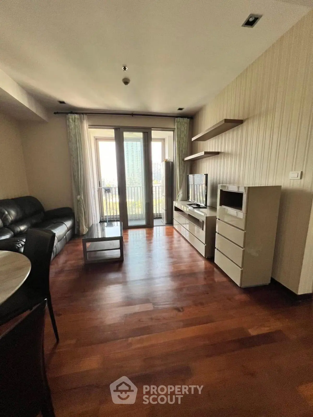 Spacious living room with modern furniture and balcony access, featuring elegant wooden flooring.