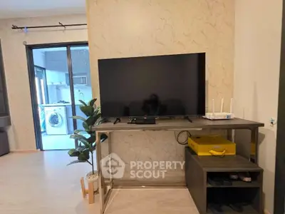 Modern living room with TV and view into a sleek kitchen with washing machine.