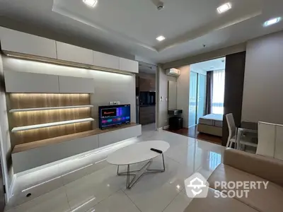 Spacious modern living room with glossy white floors, elegant lighting, and a sleek entertainment unit, leading to a cozy bedroom.