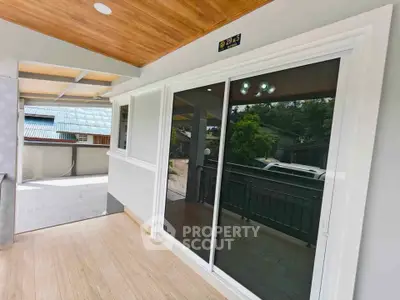 Modern balcony with sliding glass doors and wooden ceiling, offering a serene outdoor view.
