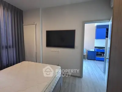 Modern bedroom with wall-mounted TV and view into a stylish kitchen