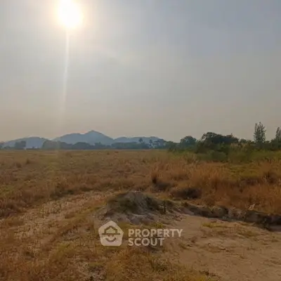Expansive land with scenic mountain views under a bright sun, perfect for development.