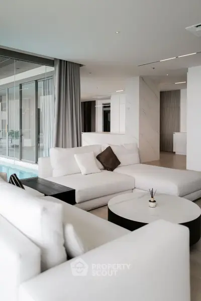 Luxurious modern living room with white sofas and pool view, perfect for relaxation.