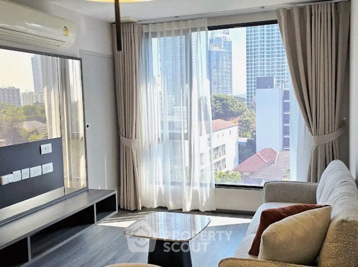 Modern living room with large windows offering stunning city views, featuring cozy seating and elegant decor.