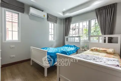 Bright bedroom with twin beds, large windows, and air conditioning unit.