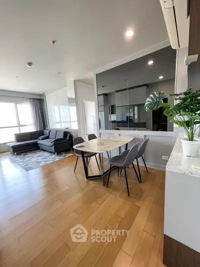 Modern living room with dining area and large windows, featuring sleek furniture and wooden flooring.