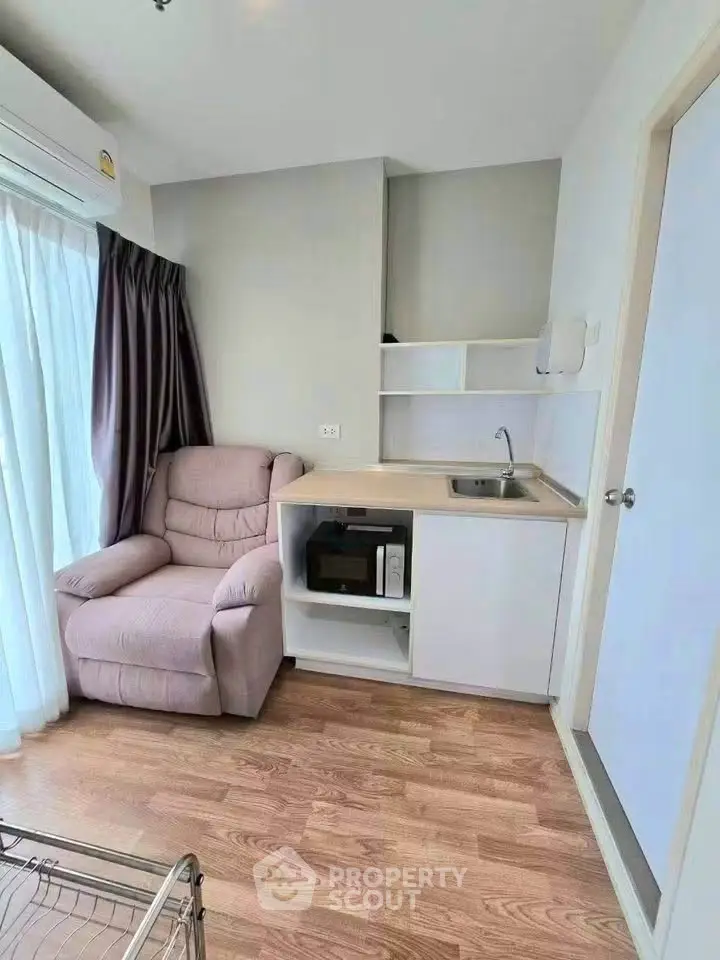 Cozy living space with armchair, kitchenette, and natural light from large window.