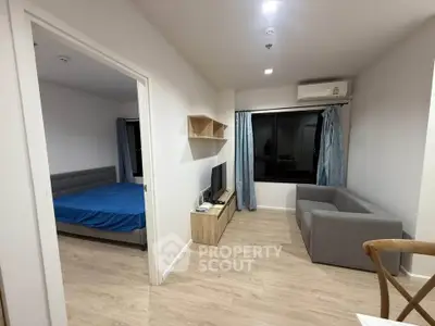 Modern apartment living room with cozy sofa and TV, adjacent to a bedroom with a blue bedspread.