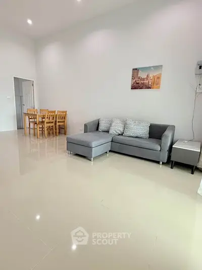Spacious living room with modern gray sofa and dining area, perfect for family gatherings.