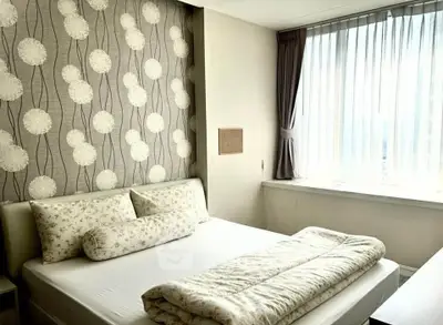 Cozy bedroom with elegant wallpaper and natural light through large window.