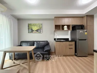 Modern living room with kitchenette, featuring sleek wooden cabinets and cozy black leather sofa.